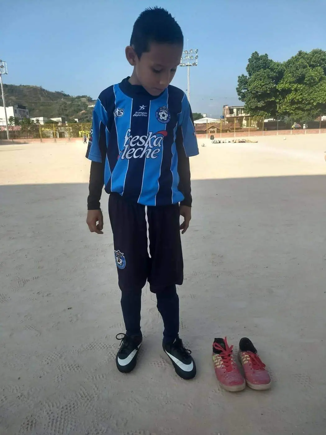 Young soccer player looking at his new cleats next to old shoes on a dusty field.
