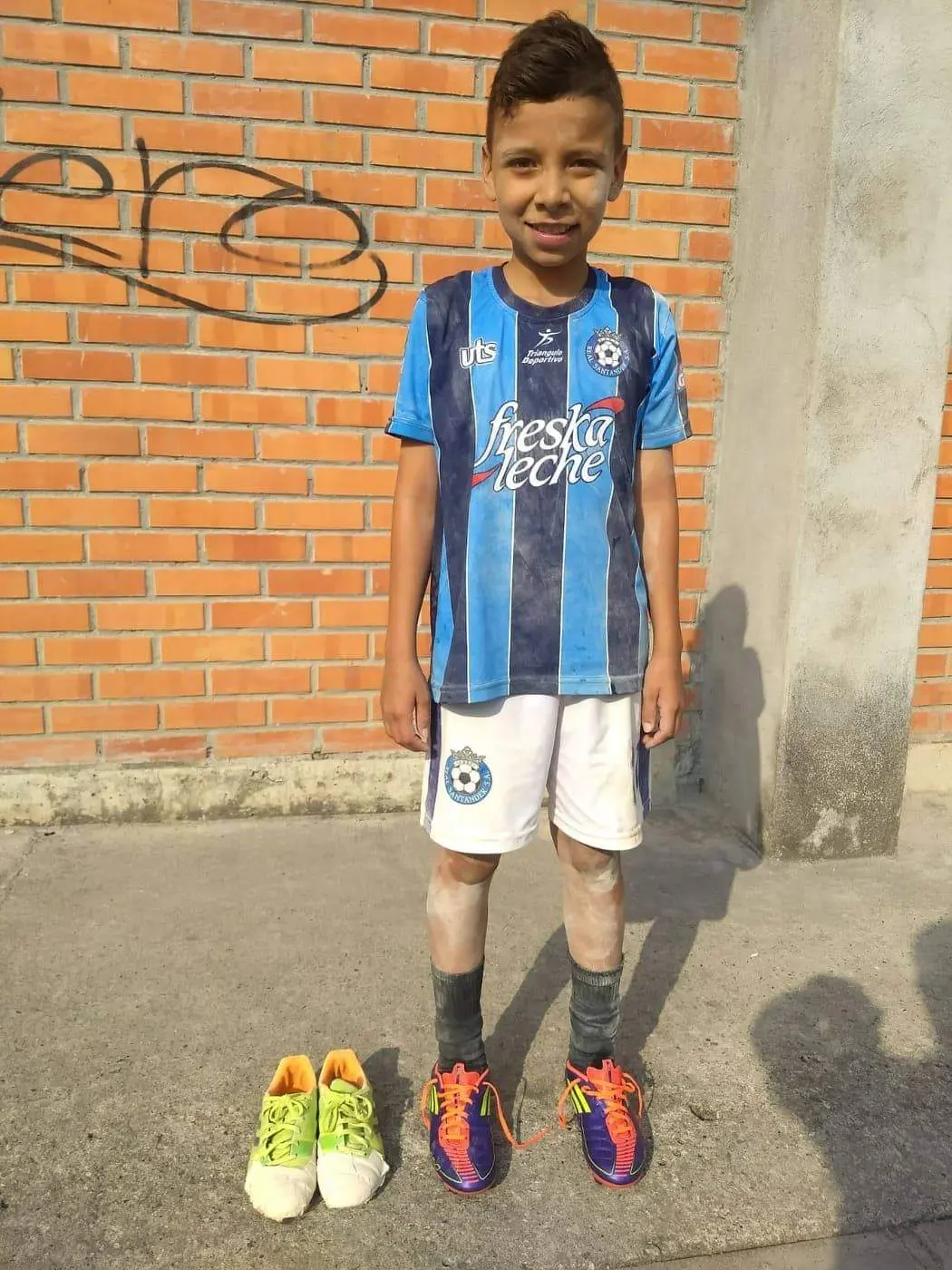 Young boy in soccer gear with two pairs of shoes, one worn and one new.